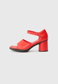 Red leather sandal with an open toe, featuring a wide strap over the foot and an ankle strap. The heel is a chunky, cylindrical shape.