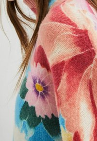 Suéter tejido colorido con patrones florales en tonos rosa, azul y verde. Textura suave con escote redondeado y diseño ajustado.