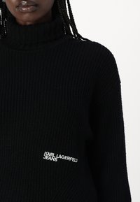 Schwarzer gerippter Strickpullover mit weitem Schnitt. Mit weißem gesticktem Logo "KARL LAGERFELD JEANS" auf der Vorderseite.