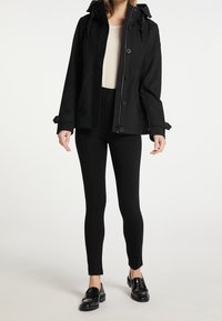 Mustat vedenpitävät takki hupparilla, jossa on suuria nappeja ja säädettävät hihansuut, yhdistettynä mustiin leggings-housuihin ja kiiltäviin mustiin loafer-kenkiin.