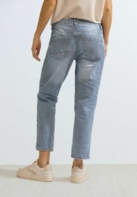 Blå- och vitrandiga jeans med rak passform, fem fickor och midjehögt liv, tillsammans med beige sneakers.