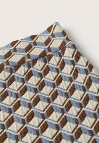 Tissu avec un motif géométrique de cubes entrelacés en bleu, marron et beige, montrant la texture et les détails de couture.