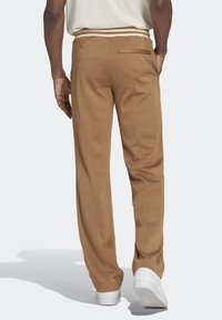 Bruna skräddarsydda byxor i en strukturerad väv, med sidsömmar och en bakficka. Byxorna har en vit accentuerad midja och är matchade med vita skor.