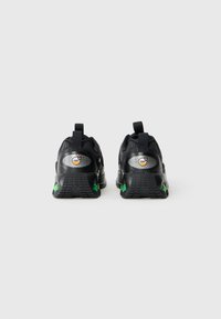 Sapatilhas de desporto pretas com parte superior em malha texturizada e detalhes verdes. Apresentam uma sola acolchoada e uma alça para facilitar o calçar.