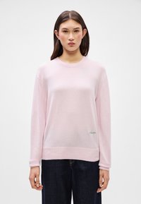 Ρροζ πουλόβερ με μακριά μανίκια, στρογγυλή λαιμόκοψη και ριμπ μανσέτα. Διαθέτει διακριτό πράσινο λογότυπο στην αριστερή πλευρά. Μαλακή υφή και ελαφρύ σχέδιο.