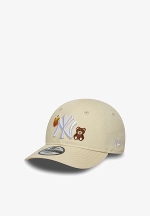 Beige Baseballkappe mit einem gebogenen Schild, ausgestattet mit dem weißen New York Yankees-Logo sowie gestickten Patches von einem Bären und Pommes frites auf der Vorderseite.