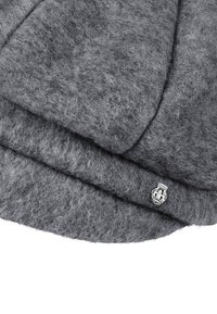 Folded gray wool felt hat with a small metallic emblem featuring a detailed crest attached near the brim.