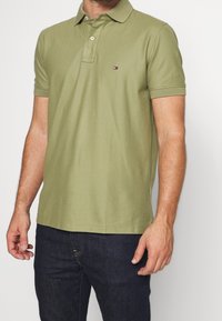 Polo vert olive en coton doux, avec un col classique, des manches courtes et un petit logo sur la poitrine gauche.