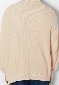 Cardigan beige en tricot avec un motif de côtes texturé, des épaules tombantes et un ourlet large. Matériau doux avec une coupe décontractée, sans fermetures visibles.
