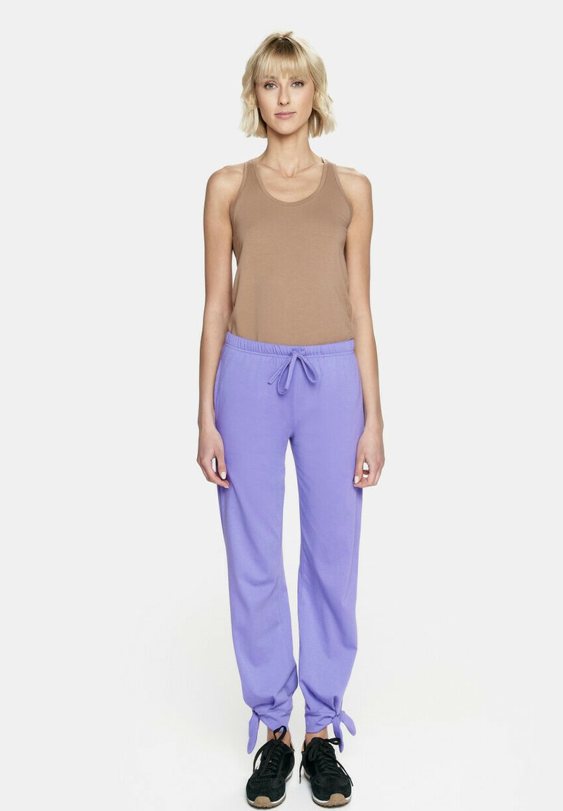 Beżowy top bez rękawów i lawendowe dresy z troczkami, z tapered nogawkami i wiązaniami przy kostkach. Czarne sneakersy dopełniają cały strój.