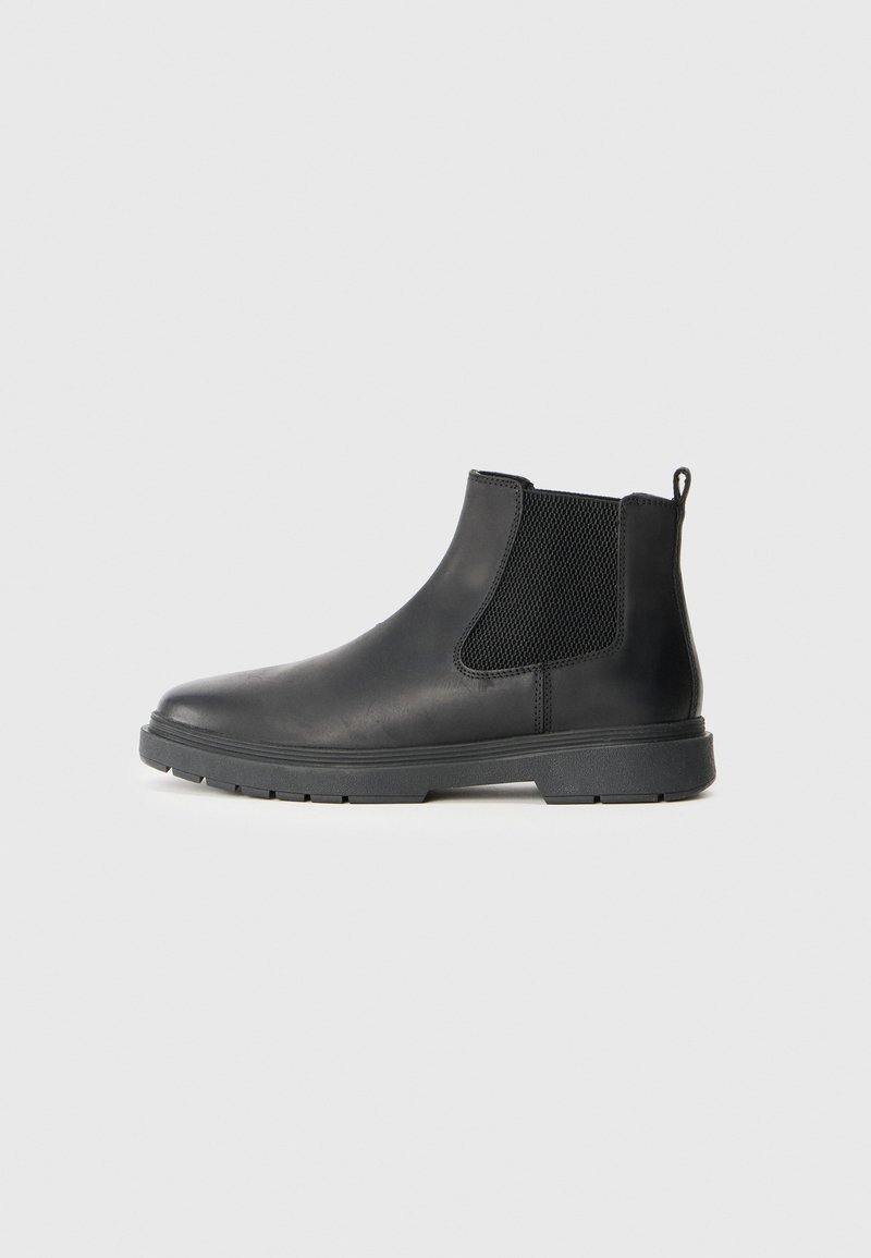 Bottines Chelsea en cuir noir avec des panneaux élastiques sur les côtés, une languette à l'arrière et une semelle en caoutchouc robuste pour une meilleure adhérence. Texture lisse.