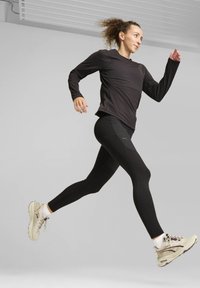 Top de manga larga negro y leggins negros combinados con zapatillas de running de color claro, con un diseño texturizado y una cinta de cintura curva.