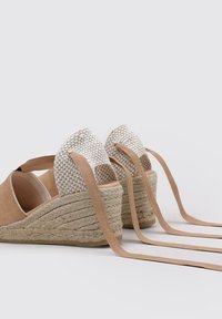 Sandalias de cuña con parte superior de ante beige, tacón de tela trenzada y largas cintas de atar beige. Presentan una suela de esparto texturizada.