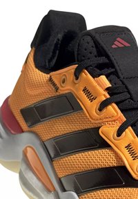 Gros plan sur une chaussure de sport orange et noire avec tissu en maille, lacets noirs et semelle grise rembourrée avec des détails orange.
