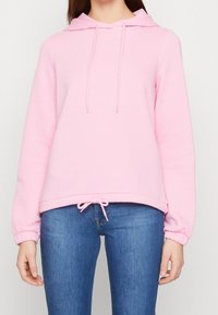 Felpa rosa con cappuccio, coulisse, polsini a coste e una vestibilità ampia, abbinata a jeans blu. Tessuto morbido, design casual.