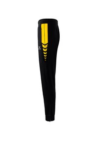 Zwarte sportbroek met een gele streep aan de linkerkant, voorzien van een tapers ontwerp, zijzakken en ritsen bij de enkels.