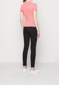 Różowy dziergany krótki top z wzorem warkocza, w zestawieniu z czarnymi obcisłymi dżinsami i białymi trampkami, widziany od tyłu.