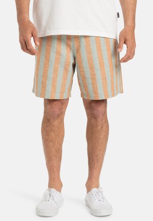Shorts rayés en mélange de lin bleu clair et orange. Avec des rayures verticales, une coupe décontractée et des poches latérales. Portés avec des baskets blanches.