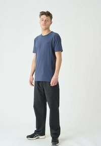 Dunkelblaues Baumwoll-T-Shirt mit rundem Halsausschnitt, kurzen Ärmeln und einem kleinen Logo auf der Brust, kombiniert mit schwarzen Hosen und Turnschuhen.