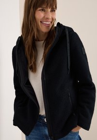 Veste en polaire noire à zip avec capuche, dotée de poches latérales, d'un tissu texturé et d'une doublure intérieure noire contrastante.