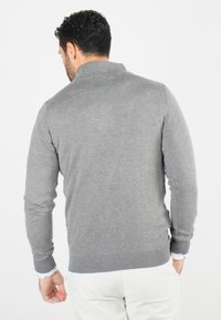 Pull en tricot gris avec des manches longues, des poignets côtelés et un col montant, présentant une texture lisse et une coupe ajustée.