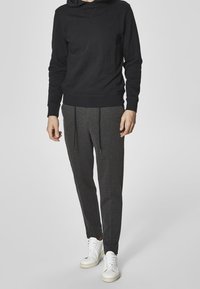 Czarna bluza z kapturem z długimi rękawami w połączeniu z ciemnoszarymi spodenkami dresowymi z troczkami, noszona z białymi sneakersami.