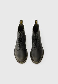 Bottines en cuir noir jusqu'à la cheville avec bouts ronds, six œillets, coutures jaunes et une languette de tirage jaune au talon. Finition de surface texturée.