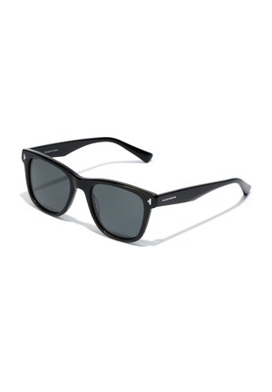 Black rectangular sunglasses with dark lenses, slim arms, and white branding on the temples, placed on a white surface.