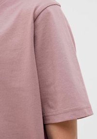 Kurzärmliges T-Shirt aus mauvefarbenem Baumwollstoff mit glatter Textur und Rundhalsausschnitt. Saum und Ärmelabschlüsse zeigen saubere Nähdetails.