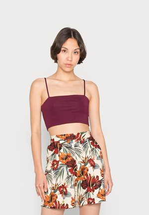 Top cropped bordeaux com alças finas, combinado com calções de cintura alta que apresentam um padrão floral em vermelho, laranja e verde sobre um fundo-creme.