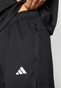 Μαύρο αθλητικό σορτς με διάτρητη υφή, ελαστική μέση και τσέπη με φερμουάρ. Διαθέτει λευκό τρίγωνο λογότυπο.