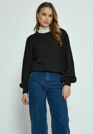 Maglione nero con collo tondo e maniche lunghe a sbuffo, abbinato a jeans in denim blu a vita alta. Tessuto morbido, design casual.