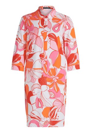Donna che indossa un abito al ginocchio con grandi motivi floreali rosa, arancio e bianchi e sandali rosa con tacco a blocco e punta aperta.