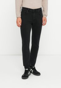 Jeans de denim negro con un corte ajustado, que cuentan con cinco bolsillos, un cierre de botón y detalles de costura sutiles. Combinados con zapatillas negras.