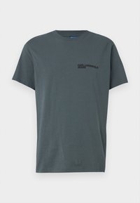 Grå bomulls t-shirt med rund halsringning och korta ärmar. Har en svart logotyptryck på vänster bröst. Enkel, rak skärning.