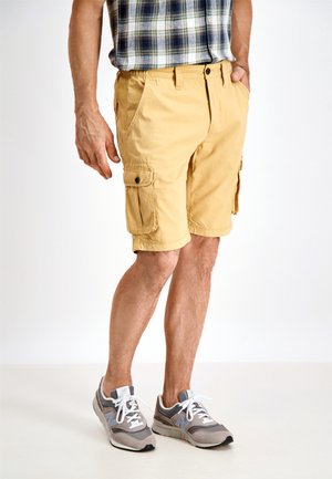 Gule cargo shorts med sidelommer, lavet af letvægtsstof, med en afslappet pasform og en ensartet tekstur. Kombineret med grå sneakers.