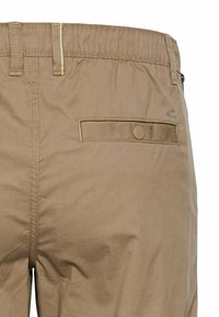Beige cargo bukser med elastisk talje, baglomme med knaplukning og kontrasterende sy detaljer. Blødt, holdbart stof.