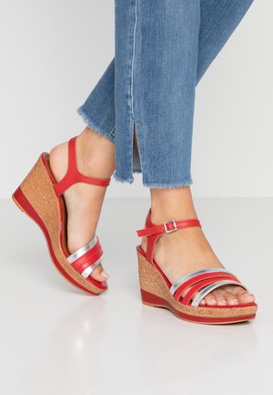 Czerwone sandały na koturnie z srebrnymi paskami i korkowymi detalami. Posiadają zamknięty tył oraz pasek na kostkę z regulowaną klamrą. Idealne na codzienne noszenie.