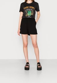 Zwarte graphic t-shirt met "Dark Rebel" ontwerp, gecombineerd met zwarte shorts met elastische taille en chunky zwarte platform sandalen.