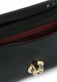 Clutch in pelle nera con texture liscia, chiusura con ferramenta dorata e fodera color bordeaux visibile attraverso la cerniera aperta.