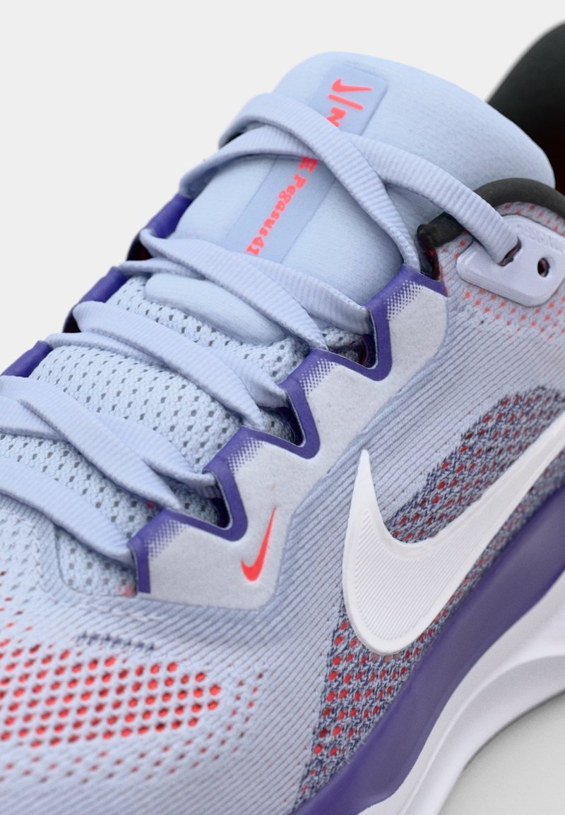 Zapatilla de running de Nike con parte superior de malla azul claro, acentos morados, paneles texturizados, punta redondeada, cordones planos y destacado logo de swoosh blanco.