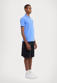 Lyseblå polo med krage, kombinert med svarte shorts. Outfiten er fullført med hvite sneakers og hvite sokker. Minimalistisk design.