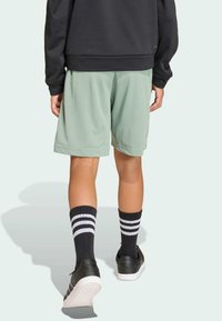 Osoba v svetlozelených šortkách, čierno-bielych pruhovaných ponožkách, čiernych teniskách a čiernej mikine, z pohľadu zozadu.