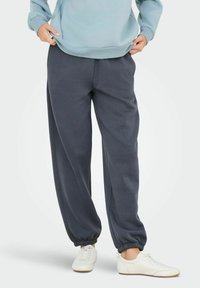 Pantaloni della tuta grigio scuro con vestibilità comoda, polsini affusolati, vita elastica e texture morbida, abbinati a sneaker bianche.