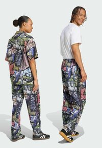 Zwei Models tragen passende Outfits mit grafischen Drucken. Das Hemd hat ein mehrfarbiges Muster. Die Hose hat Streifen und eine lockere Passform. Schwarze Schuhe runden den Look ab.