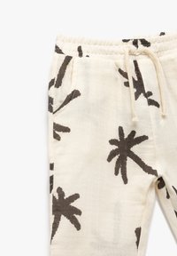 Joggingi w kolorze kremowym z czarnymi nadrukami palm, elastycznym paskiem w talii, sznurkiem do regulacji oraz bocznymi kieszeniami. Wykonane z miękkiego, oddychającego materiału.