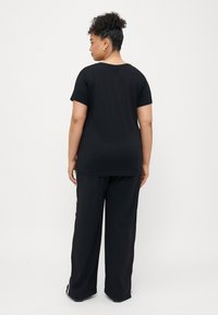 Μαύρη βαμβακερή μπλούζα κοντομάνικη, με άνετη εφαρμογή. Συνδυασμένη με φαρδύ μαύρο παντελόνι, που επιδεικνύει έναν απλό και μινιμαλιστικό σχεδιασμό.