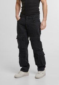 Pantaloni cargo negri din denim, cu multiple buzunare laterale, croială relaxată și o textură ușor uzată.