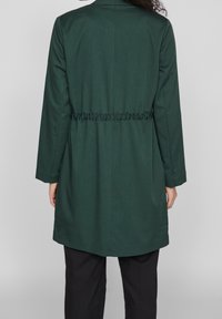 Tmavě zelený látkový kabát s dlouhými rukávy, staženým pasem a rovnými lemy. Jednoduchý design, texturovaný materiál, žádné viditelné vzory ani detaily.