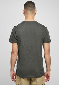 T-shirt corto a maniche corte di colore grigio scuro con scollatura a girocollo, realizzato in un tessuto morbido. Texture liscia e orlo posteriore leggermente più lungo.